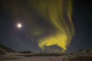 The aurora borealis glowing green over a snowy landscape at night